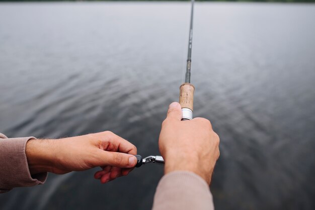 Primer plano de la mano del hombre con caña de pescar sobre el lago