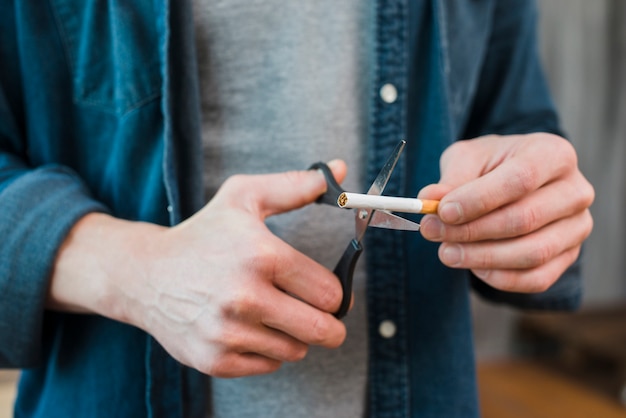 Primer plano de la mano del hombre cortando cigarrillo con tijera