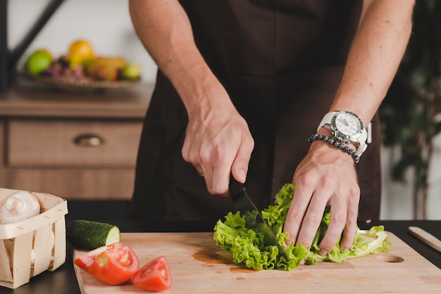 Foto gratuita primer plano, de, mano de hombre, corte, lechuga, con, cuchillo, en, tajadera