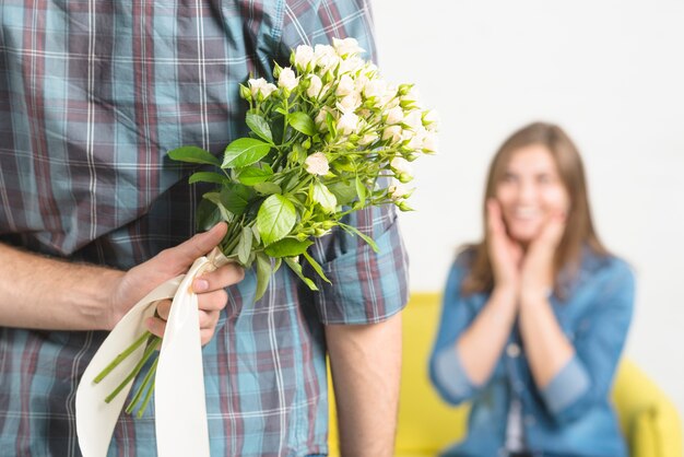 Primer plano de la mano de un hombre escondiendo flores de su novia