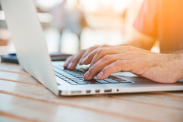 Primer plano de la mano del hombre escribiendo en la computadora portátil sobre el escritorio de madera