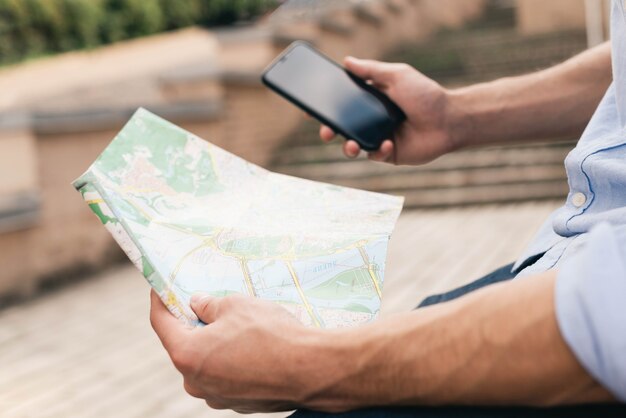 Primer plano de la mano del hombre con mapa y teléfono celular al aire libre