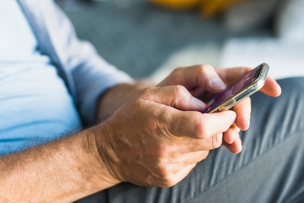 Primer plano de la mano del hombre mayor de navegación en el teléfono móvil