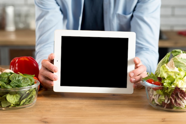 Foto gratuita primer plano de la mano del hombre mostrando tableta digital con pantalla en blanco en la cocina