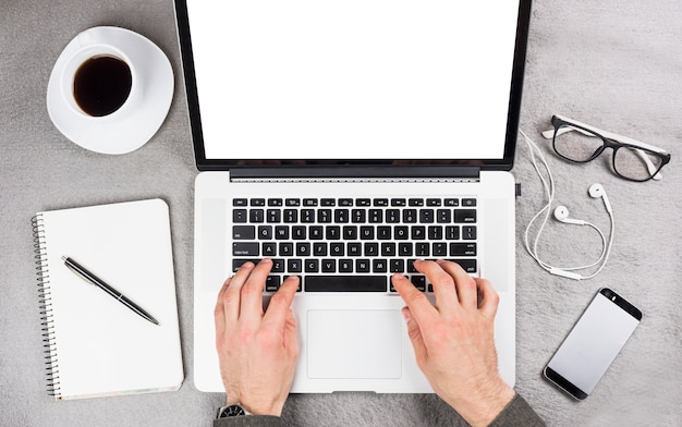 Foto gratuita primer plano de la mano de un hombre de negocios escribiendo en tableta digital con suministros de oficina y taza de café en el escritorio