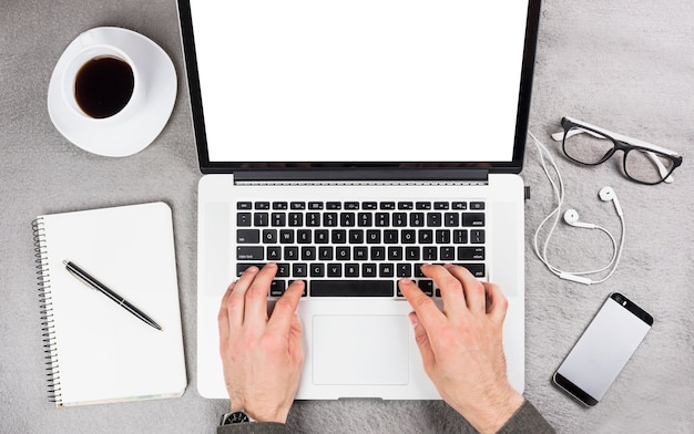 Primer plano de la mano de un hombre de negocios escribiendo en tableta digital con suministros de oficina y taza de café en el escritorio