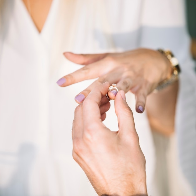 Primer plano de la mano del hombre poniendo el anillo de compromiso en el dedo de su novia