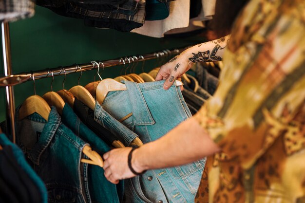 Primer plano de la mano del hombre que elige la chaqueta azul que cuelga en el carril en la tienda de ropa