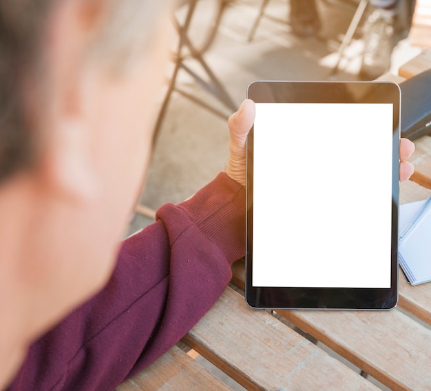 Primer plano de la mano del hombre que sostiene la tableta digital con pantalla en blanco en blanco en la mesa de madera