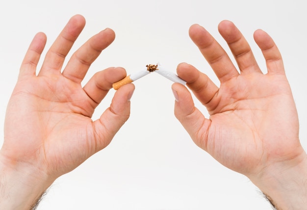 Foto gratuita primer plano de la mano de un hombre rompiendo el cigarrillo contra el fondo blanco