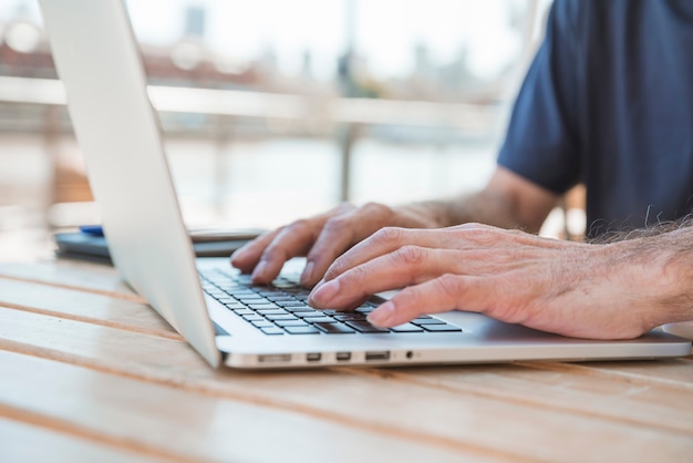 Primer plano de la mano del hombre senior escribiendo en la computadora portátil