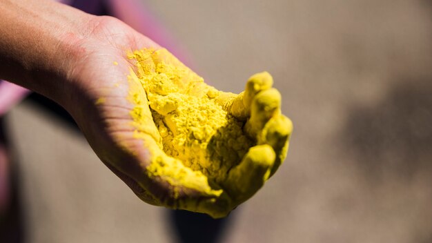 Primer plano de la mano de un hombre sosteniendo color holi amarillo