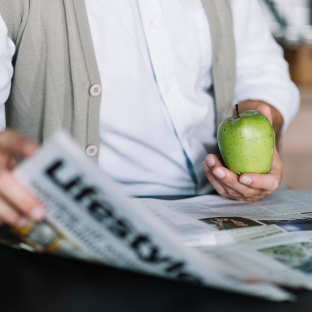 Primer plano de la mano del hombre sosteniendo periódico y manzana verde