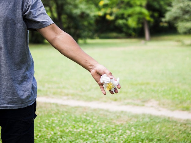 Primer plano de la mano del hombre tirando papel arrugado en el parque
