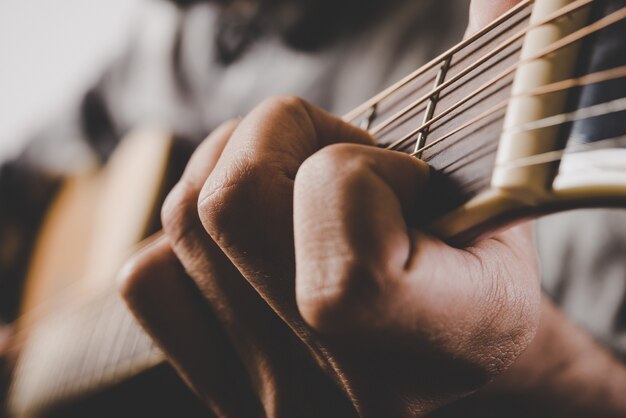 Primer plano de la mano del hombre tocando la guitarra.