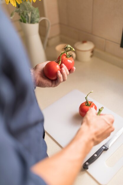 Primer plano de la mano del hombre con tomates rojos sobre tajadera