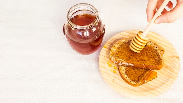 Primer plano de la mano humana esparciendo miel sobre pan con cucharón de miel
