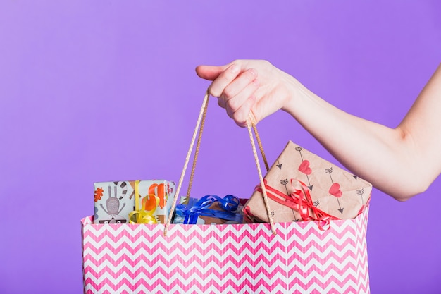 Primer plano de la mano humana que sostiene la bolsa de papel con el regalo envuelto