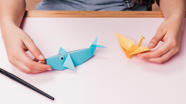 Primer plano de mano humana sosteniendo origami peces y aves