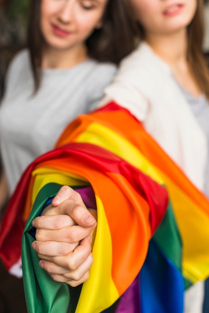Primer plano de la mano de la joven mujer lesbiana envuelta en una colorida bandera del arco iris