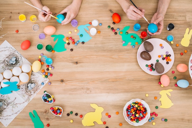 Primer plano de la mano de madre e hija pintando los huevos con pincel en el día de Pascua