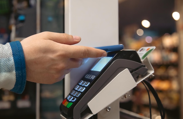 Primer plano de la mano masculina que sostiene el teléfono inteligente en la terminal de pago