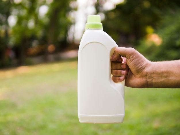 Foto gratuita primer plano de mano masculina sosteniendo una botella de detergente en el parque