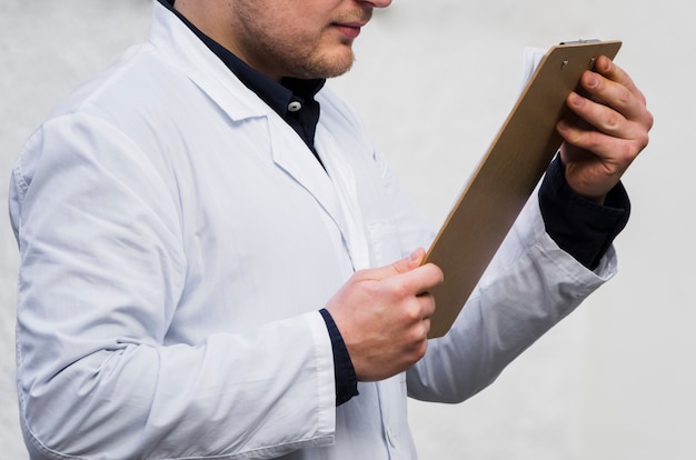 Primer plano de la mano de un médico de sexo masculino que lee el informe médico en el portapapeles