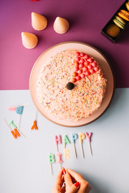 Primer plano de la mano de una mujer arreglando velas de cumpleaños sobre fondo dual