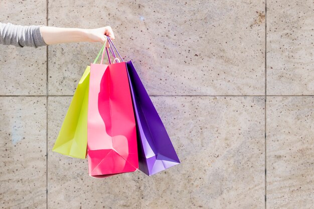 Primer plano de la mano de una mujer con coloridos bolsos de compras delante de la pared