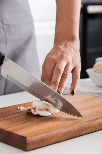 Primer plano de la mano de la mujer cortando la seta con un cuchillo en la tabla de cortar