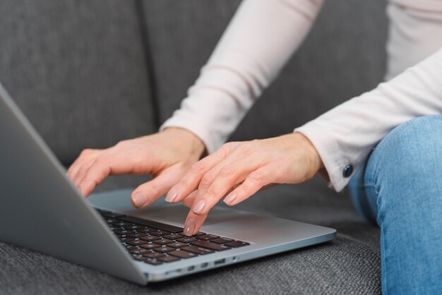 Primer plano de la mano de la mujer escribiendo en la computadora portátil sobre el sofá