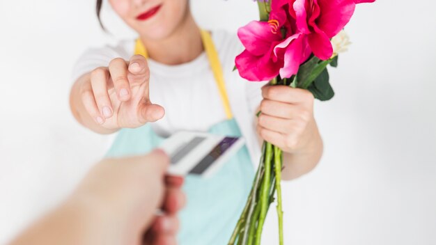 Primer plano de la mano de una mujer con flores que toman la tarjeta de crédito de su cliente