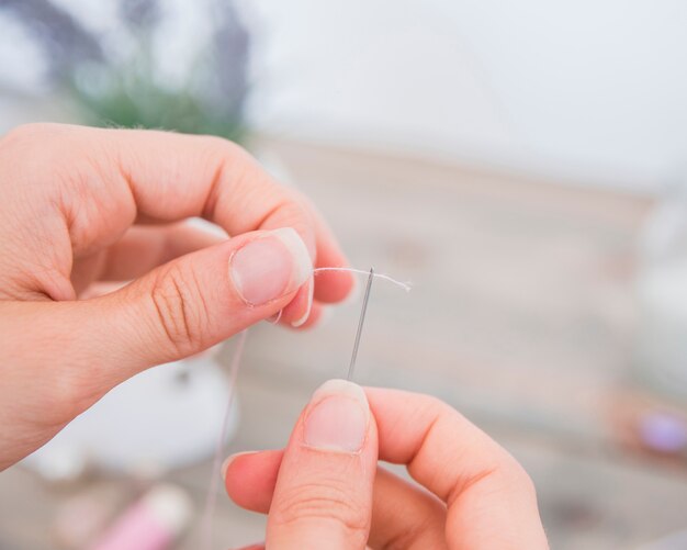 Primer plano de la mano de la mujer insertando hilo en la aguja