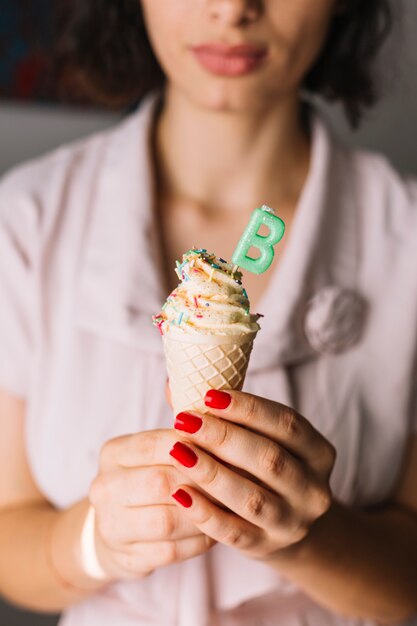 Primer plano de la mano de la mujer con letra b vela en cono de helado