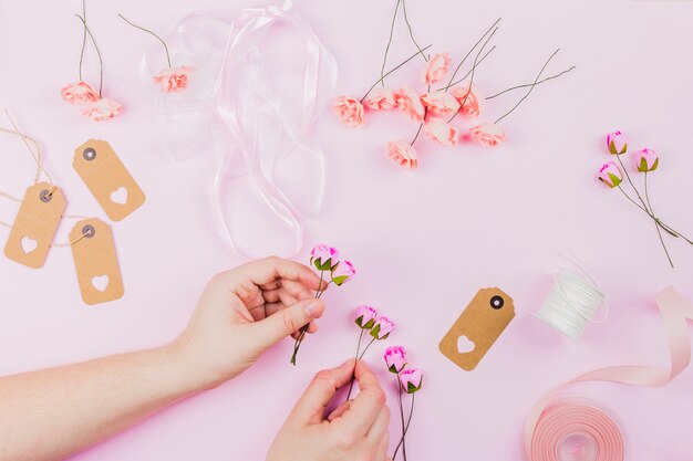 Primer plano de la mano de la mujer que arregla la flor con la cinta y las etiquetas en fondo rosado