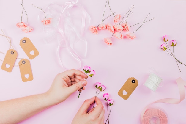 Primer plano de la mano de la mujer que arregla la flor con la cinta y las etiquetas en fondo rosado