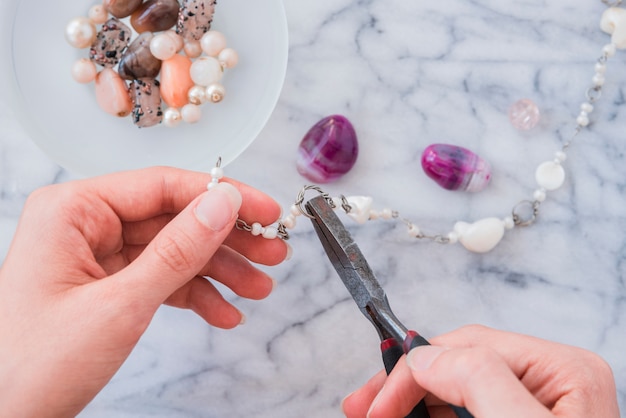 Primer plano de la mano de la mujer que fija la pulsera con alicates en el escritorio de mármol