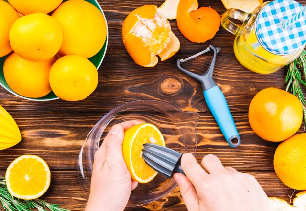 Primer plano de la mano de la mujer que hace jugo de naranja fresco en mesa de madera