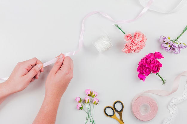 Primer plano de la mano de la mujer que hace el ramo de flores con cinta sobre fondo blanco