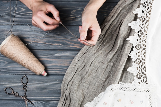 Primer plano de la mano de la mujer que inserta hilo de hilo en aguja con variedad de textiles