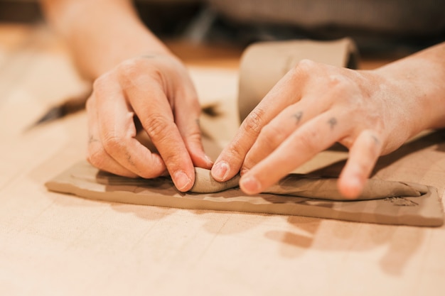 Primer plano de la mano de la mujer que moldea la arcilla en la mesa de madera