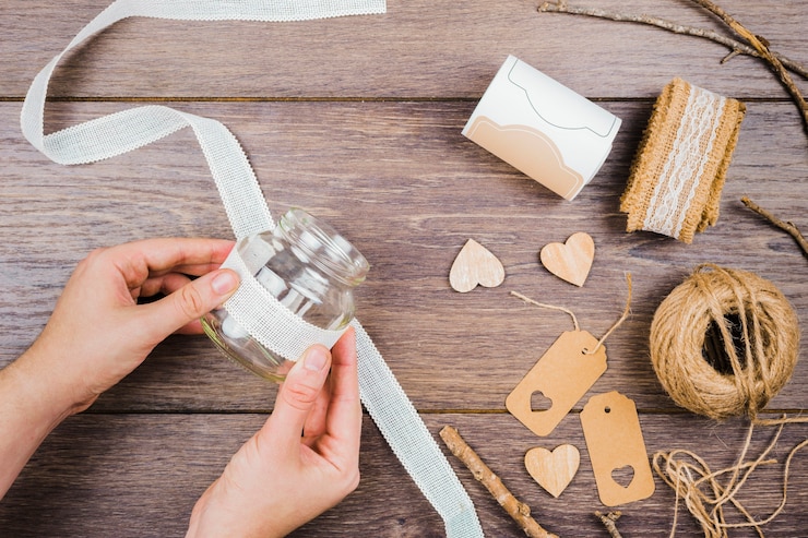 Foto gratuito primer plano de la mano de la mujer que pega la cinta de encaje blanco en una botella de vidrio sobre el escritorio de madera