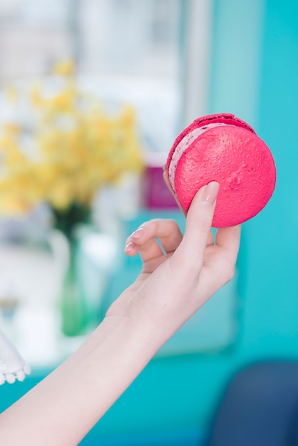 Primer plano de la mano de la mujer que sostiene el emparedado helado helado rosado contra el contexto borroso