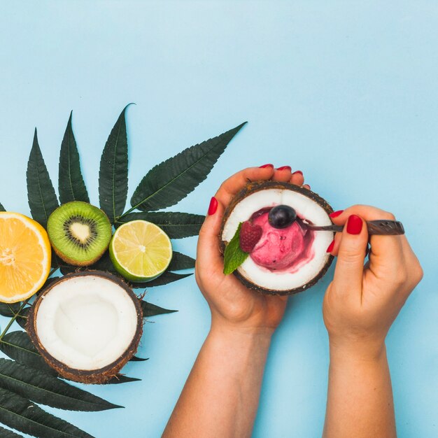 Primer plano de la mano de una mujer que sostiene helado de fruta congelada dentro del coco reducido a la mitad