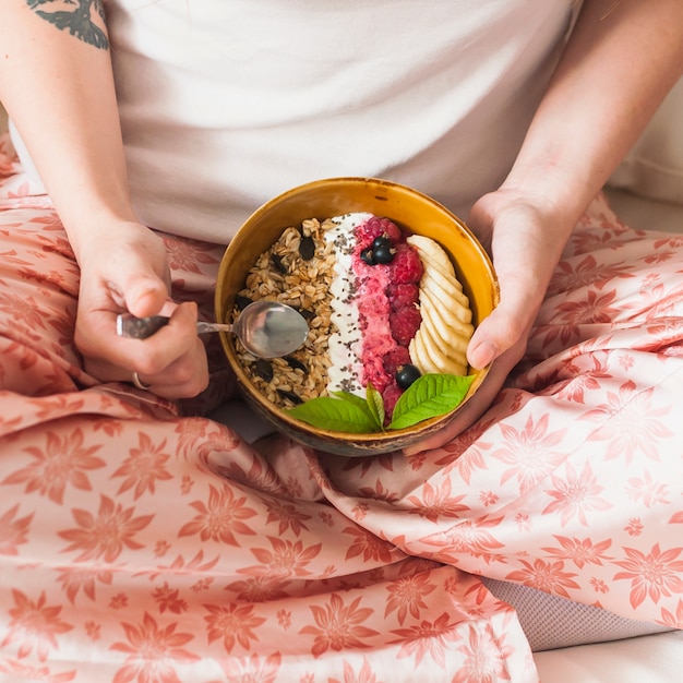 Primer plano de la mano de la mujer que sostiene el tazón de avena con frutas