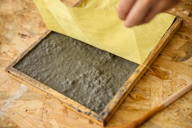 Primer plano de la mano de una mujer que sostiene la tela amarilla sobre la pulpa de papel