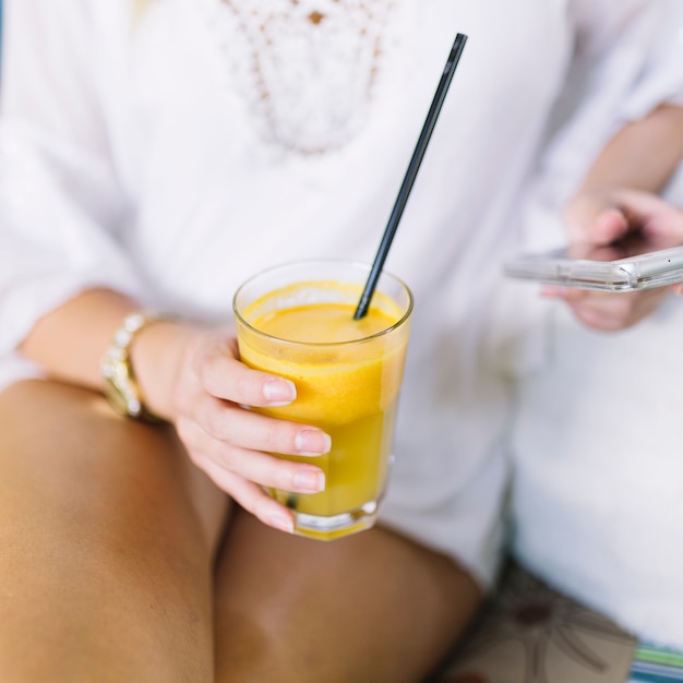 Primer plano de la mano de la mujer que sostiene un vaso de jugo usando un teléfono móvil