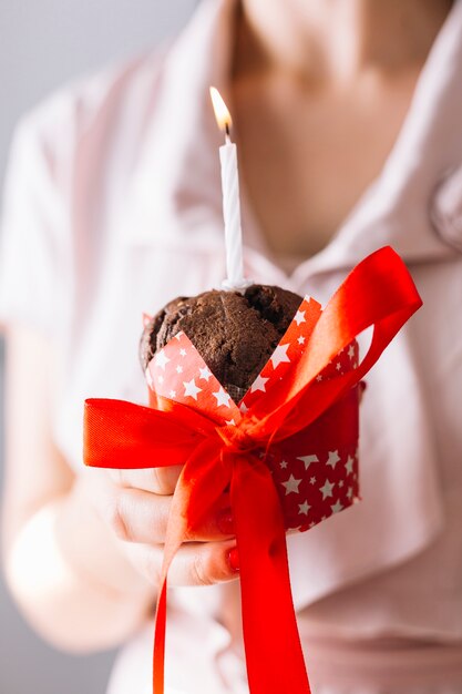 Primer plano de la mano de una mujer sosteniendo cupcake con vela iluminada