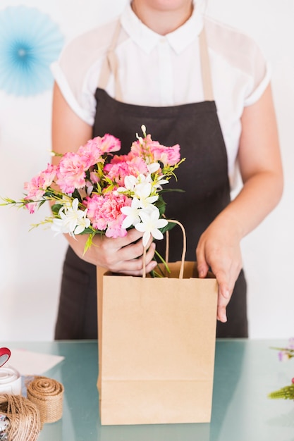 Primer plano de la mano de una mujer sosteniendo flores con una bolsa de papel en el escritorio